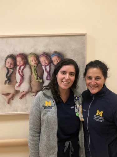 Two women standing side by side next to a picture of babies
